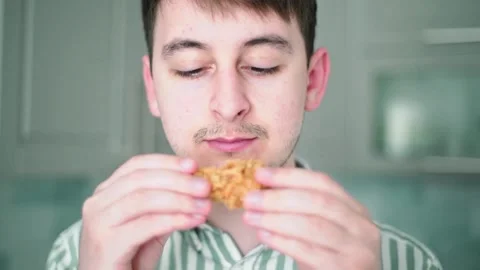 A man bites a chicken wing. Overeating and obesity. Harmful fast food Stock Footage 132355800