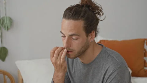 Man bites fingernails with hand to mouth on bed in bedroom, seated and slig.. Stock Footage 337377171