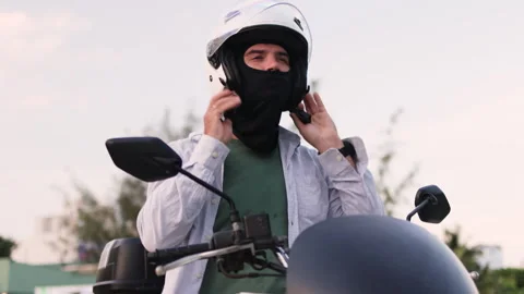 The man in a black balaclava puts on his helmet while sitting on the moped. Stock Footage 313733204