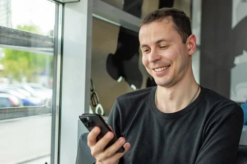 A man in a black batch jacket looks at his phone and smiles Stock Photos