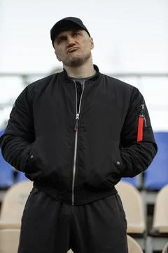 Man in black bomber jacket and cap reacts in empty stadium during intense game Stock Photos