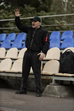 Man in black bomber jacket and cap reacts passionately in empty stadium during Stock Photos