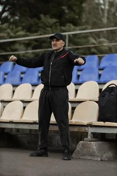 Man in black bomber jacket and cap reacts passionately in empty stadium stands Stock Photos