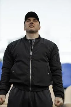 Man in black bomber jacket expresses emotions in empty stadium during team game Stock Photos