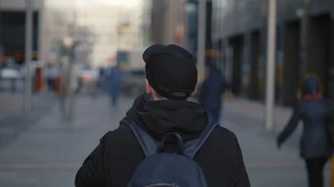 Man in black cap and backpack drinking hot coffee during walking on city street Stock Footage 86489534