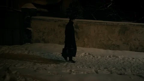 A man in a black cloak and hat walks along a wall on the sidewalk. Stock-Footage 102139084