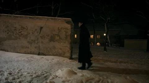 A man in a black cloak and hat walks along a wall on the sidewalk. Stock-Footage 102139272