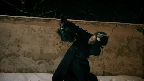 A man in a black cloak and hat walks along a wall and resisting strong wind. 스톡 동영상 102158445