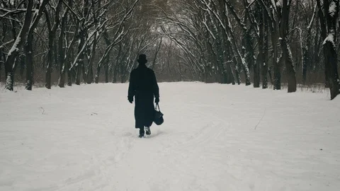 A man in a black cloak and hat walks in the park alley. 60fps. 4k Stockbeeldmateriaal 102190824