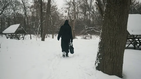 A man in a black cloak and hat walks the path in the winter forest. 60fps Stockbeeldmateriaal 102203802