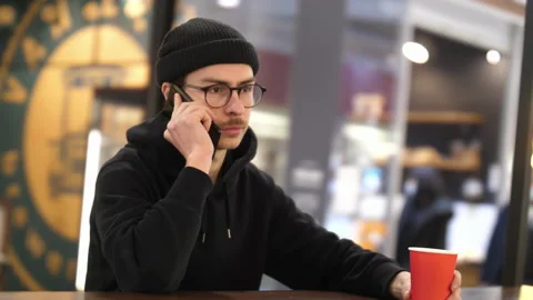 A man in black clothes and a hat is talking on the phone in a shopping mall Stock Footage 168695861