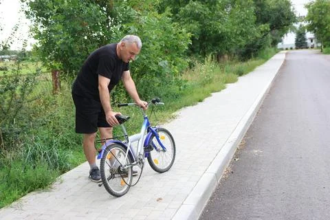 Man in black clothes checking broken chain on a kids bicycle on sidewalk near Stock Photos