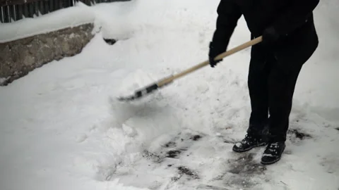 A man in black clothes cleans snow with a shovel in his yard. Winter in Russia Stock Footage 145773394