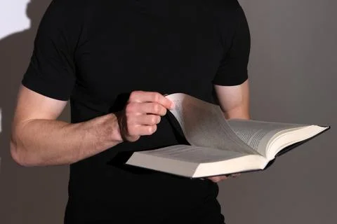 A man in black clothes flips through a book, holding it in his hands. Stock Photos