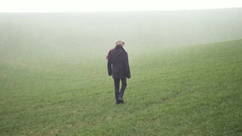 A man with a black coat walking through hail and rain storm on grass field. Video stock 145321699
