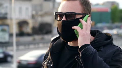 Man with black face mask walking at the street and talking on the mobile phone.  Stock Footage 129543479