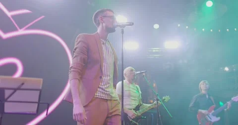 Man in black glasses with beard in jacket performs on stage with musical group Video stock 221650237