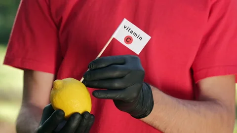 A man with black gloves inserts a "vitamin C" flag into a lemon Stock Footage 141870945