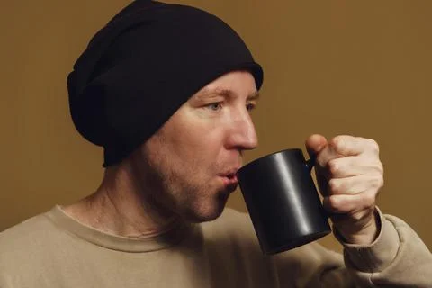 A man in a black hat drinks from a black cup, close-up Stock Photos