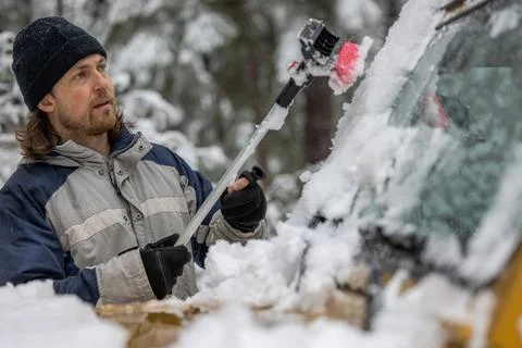 A man in a black hat is using a snow brush to clear the snow off of a car Stock Photos