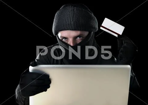 Man in black holding credit card using computer laptop for criminal activity Stock Photos