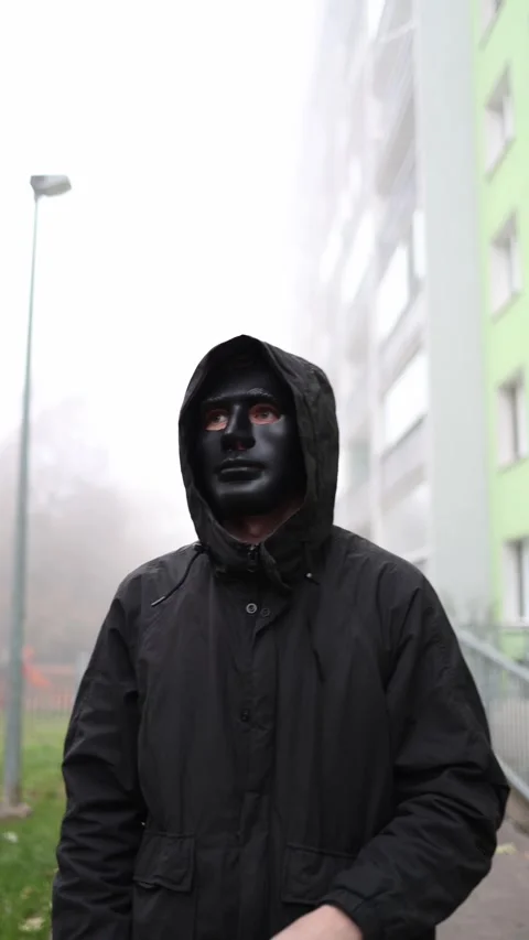 A man in a black hooded jacket adjusts a dark mask on his face, standing in an u Stock Footage 290187210