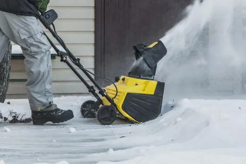 A man in a black jacket and a gray pants is brushing white snow with the yell Stock Photos