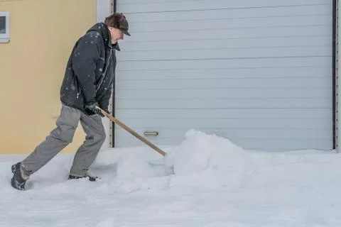 A man in a black jacket and light-colored gray pants and a brown hat cleans s 스톡 사진