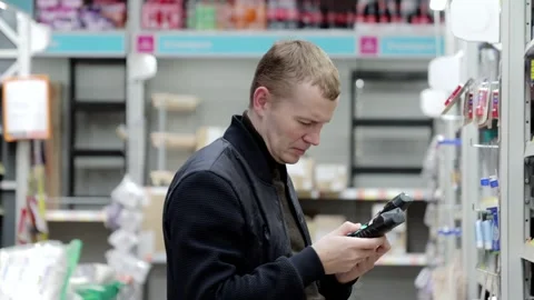A man in a black jacket compares two products in a hardware store. He holds an Stock Footage 303393143