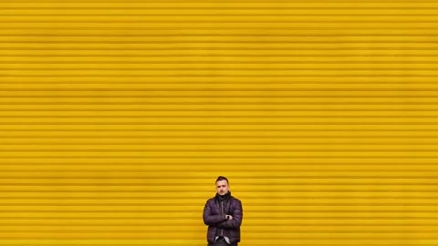 Man in black jacket crosses arms near yellow shop shutters Stock Footage 144849162