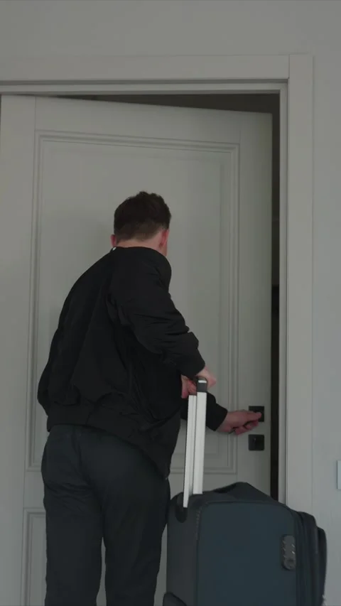 Man in black jacket enters through open door pulling rolling suitcase into Stock Footage 343083741