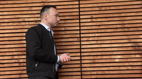 A man in a black jacket leaned on a wooden wall Stock Footage 126553365