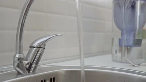 A man in a black jacket opened a tap with water in the kitchen against the Stock Footage 201946249