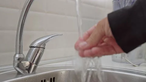 A man in a black jacket opens a tap of water to rinse his hands in the sink Stock Footage 201946416