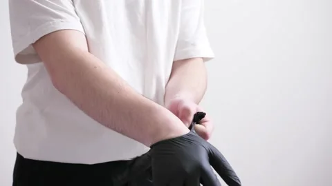 A man in black jeans and basic white t-shirt takes and wear black gloves Stock Footage 162502721