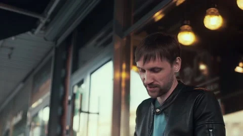A man in a black leather jacket, next to the cafe and looks down. Video stock 99914988