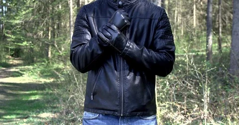 Man in black leather jacket Putting on black gloves in forest 動画素材 74691438