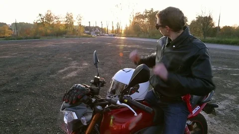 Man in black leather jacket sits on motorcycle and puts on white helmet Stock Footage 81492686