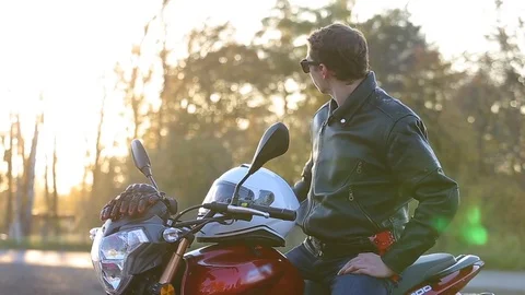 Man in black leather jacket sits on motorcycle and puts on white helmet Stock Footage 81493221