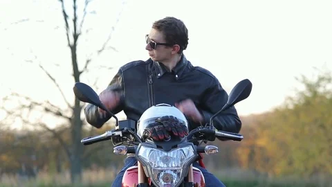 Man in black leather jacket sits on motorcycle and puts on white helmet Stock Footage 81493293