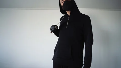 A man in a black mask waves a knife in front of the camera menacingly. Serious a 库存影片 129556162