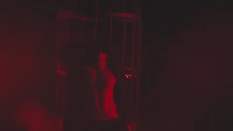 Man in black in red light in smoke near the metal cage Stock Footage 149199708