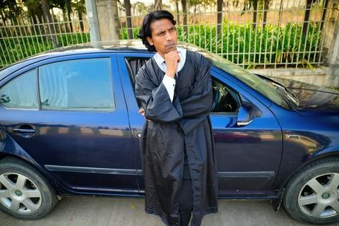 Man in black robe thinking next to blue car Stock Photos