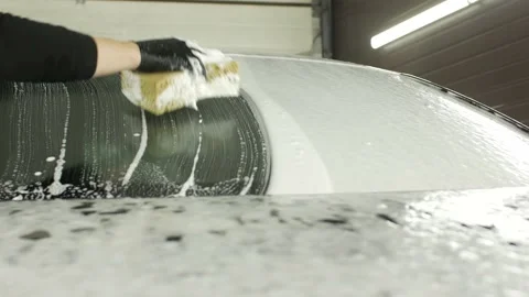 Man in black rubber gloves washes car with soapy sponge in garage. Stock Footage 195508125