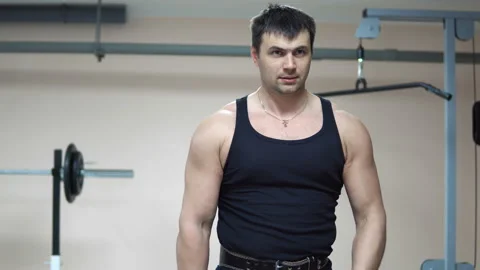 A man in a black singlet is training biceps with dumbbells. Stock Footage 91060079