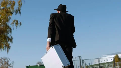 Man in black suit and hat with silver case goes to meeting to transfer money Stock Footage 129486330