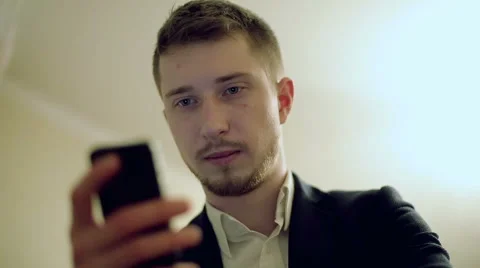 The man in a black suit with seriously face is typing something on the mobile ph Stock Footage 62927557
