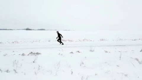 A man in black tracksuit is running along a snowy road. Winter, around the snow Stock Footage 101714259