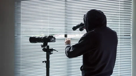 The man in black walks to the window and looks binoculars through the blinds. 库存影片 97701305