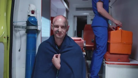 Man in blanket sit in ambulance car in blanket and smile. Stock Footage 116974633